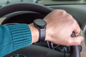 The man's hand holds the steering wheel, the watch is on his hand.